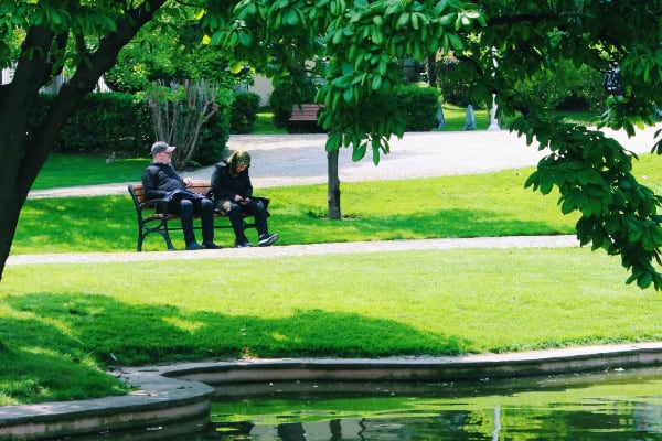 Žmonės parke sėdi ant suoliuko netoli vandens